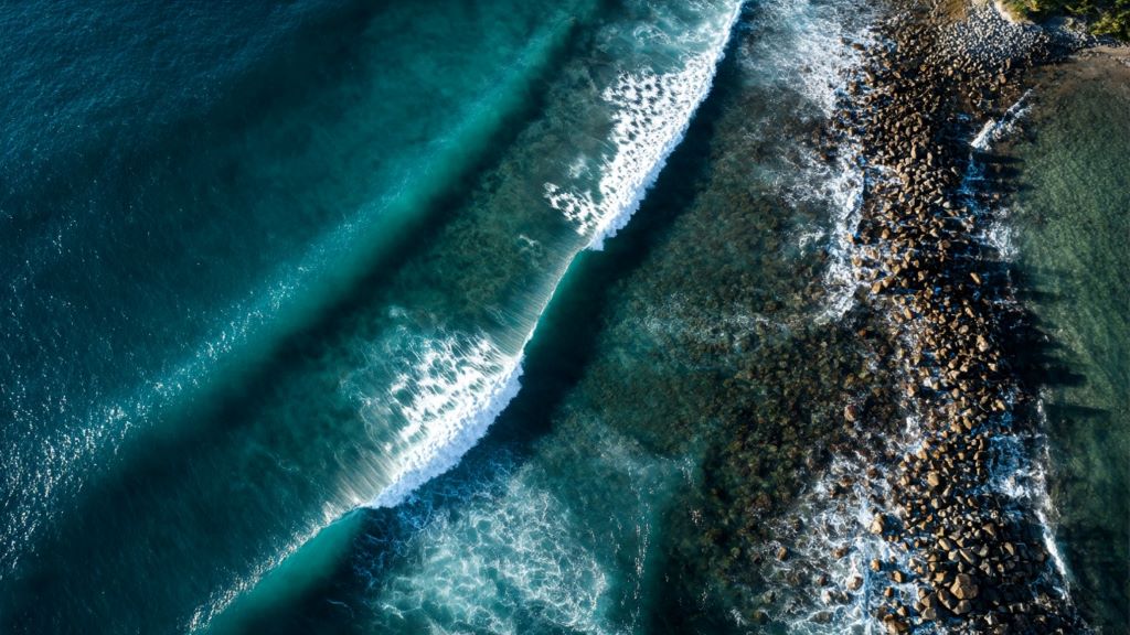 2. Aerial view of uncrowded winter surf break with clean offshore waves rolling into rocky coastline